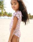 Young girl in a floral swimsuit standing on a beach with palm trees in the background