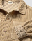 Close-up of a beige corduroy button-up shirt with a striped inner collar lining and a chest pocket, shown on a light neutral background.