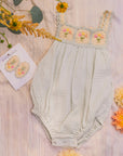 Baby romper with floral embroidery on a wooden surface with flowers around