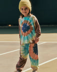 Child wearing a tie-dye outfit with a beanie on a beach.