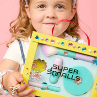 Child holding a 'Super Smalls' product set against a pink background
