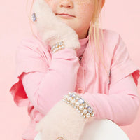Child wearing pink coat and embellished gloves against a pink background