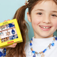Young girl wearing a blue and gold necklace with a box of jewelry against a light blue background