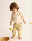 Child wearing a 'Good Day' shirt and yellow striped pants on a white background with lemons and a basket.
