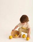 Child playing with lemons and a basket on a light background