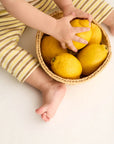 Child's hands reaching into a basket of lemons on a light surface