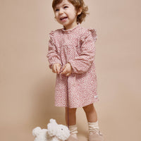 Child in a pink floral dress standing next to a white plush toy on a beige background