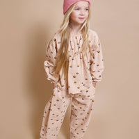 Young girl wearing a pink patterned outfit with a matching hat on a beige background