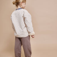 Child wearing a patterned shirt and brown pants on a beige background