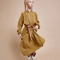 Girl wearing a mustard yellow dress with a belt on a beige background