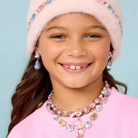 Young girl wearing a pink beanie and jewelry set against a light blue background