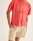 Person wearing a red 'GOOD DAY' t-shirt and striped shorts on a plain background
