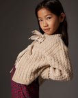 Young girl wearing a beige knitted cardigan against a dark background