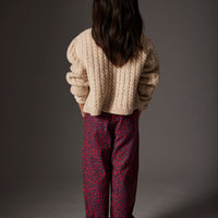 Person wearing a beige sweater and red patterned pants standing against a gray background