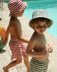 Two children in swim hats and striped swimsuits by a pool.