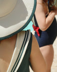 Person wearing a straw hat and a sleeveless dress with green stripes on a beach.
