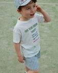 Child wearing a cap and t-shirt with text on a grassy background