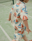 Child wearing a towel with sailboat pattern on a tennis court