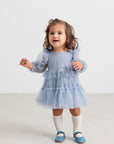 Child wearing a blue dress with long sleeves on a white background