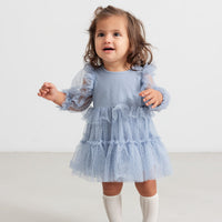 Child wearing a blue dress with long sleeves on a white background