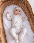 Baby in a white outfit with polka dots lying in a wicker crib.