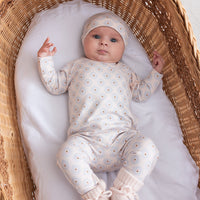 Baby in a white outfit with polka dots lying in a wicker crib.