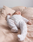 Baby in a white onesie with small patterns lying on a pink bed.