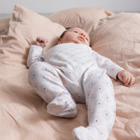 Baby in a white onesie with small patterns lying on a pink bed.