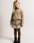 Young girl wearing a beige sweater and skirt with brown boots on a white background
