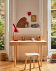 Wooden desk with a red lamp, books, and small decorative items in a room with large windows.