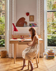 Child sitting at a desk in a bright room with large windows and greenery outside