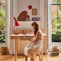 Child sitting at a desk in a bright room with large windows and greenery outside
