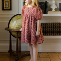 Young girl in a pink dress standing in a room with a bookshelf and globe.