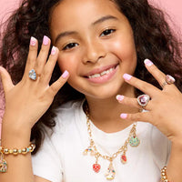 Young girl wearing multiple pieces of jewelry including rings and a necklace on a pink background