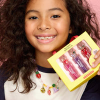 Young girl holding a yellow box with lip balms against a pink background