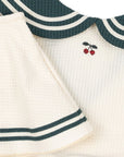 Close-up of a baby outfit with green trim and cherry design on a white background