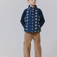 Child wearing a blue patterned vest over a dark sweater with brown pants on a white background