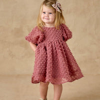 Young girl in a pink dress with a floral headband against a beige background