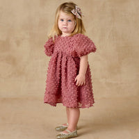 Young girl wearing a pink dress with ruffled sleeves against a beige background