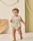 Baby in a floral romper standing against a neutral background