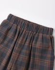 Close-up of a plaid skirt with an elastic waistband, featuring a dark gray and rust brown tartan pattern, shot against a plain white background.