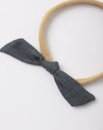 A beige fabric headband with a dark gray fabric bow tied at the front, photographed on a clean white background.