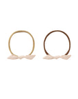 Two elastic hair ties with fabric bow accents, shown side by side on a plain white background. One hair tie is a light tan color with a pale pink bow, and the other is a medium brown with a light pink bow.