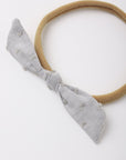A light gray textured fabric bow headband with a tan elastic band, photographed on a clean white background.