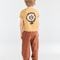 Child wearing a yellow t-shirt with a lion graphic and brown pants on a white background