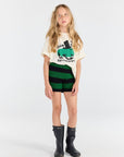 Young girl wearing a graphic t-shirt, striped shorts, and rain boots on a white background