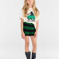 Young girl wearing a graphic t-shirt, striped shorts, and rain boots on a white background