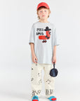 Child wearing a white t-shirt with a graphic design and colorful pants on a white background