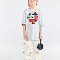 Child wearing a white t-shirt with a graphic design and colorful pants on a white background