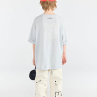 Person wearing a light blue oversized shirt, white pants with black patterns, and a red cap on a white background